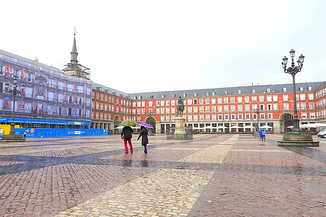 Plaza Mayor in Madrid on a rainy day, with its red-ochre façades, the equestrian statue and people with umbrellas
