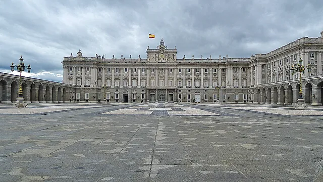 The long main façade of the Royal Palace of Madrid seen across the Plaza de la Armería under a grey sky