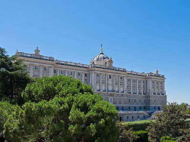The Royal Palace of Madrid between trees under a clear blue sky