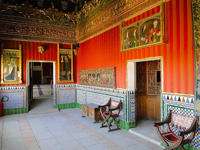 A room of the Alcázar of Segovia, with red striped walls, tiled panels and painted portraits